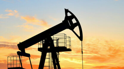 A silhouette of a pump jack system with the sun setting in the background.