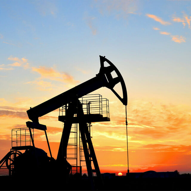 A silhouette of a pump jack system with the sun setting in the background.