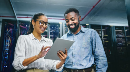 Two people in a server room looking at a tablet, both smiling.