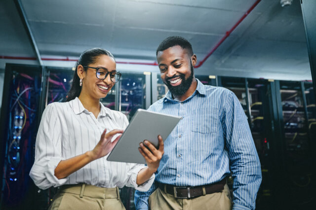 Two people in a server room looking at a tablet, both smiling.