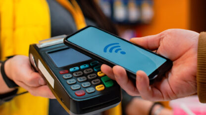 A person holds a smartphone near a payment terminal indicating a contactless payment.