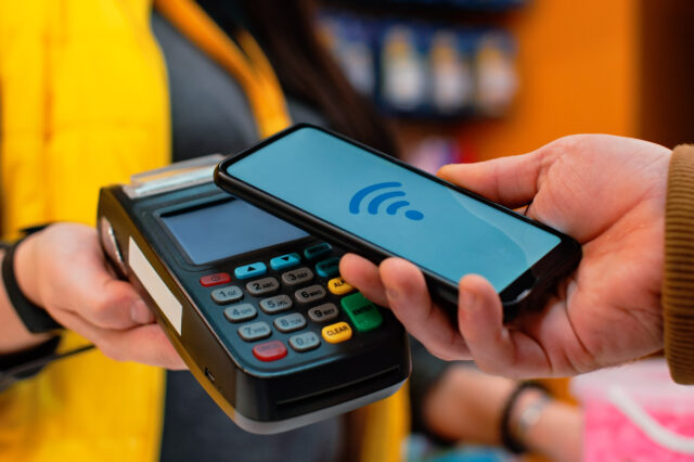 A person holds a smartphone near a payment terminal indicating a contactless payment.