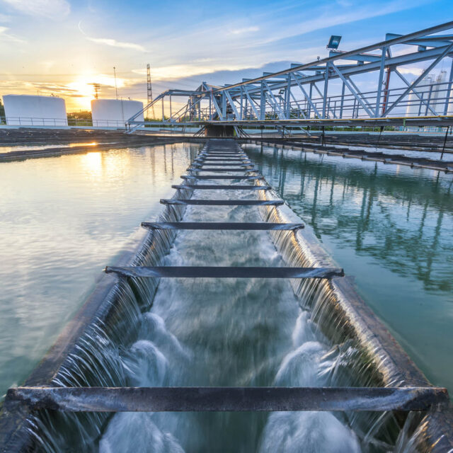 A large water treatment facility with cascading water flowing through a series of structures and tanks at sunset.