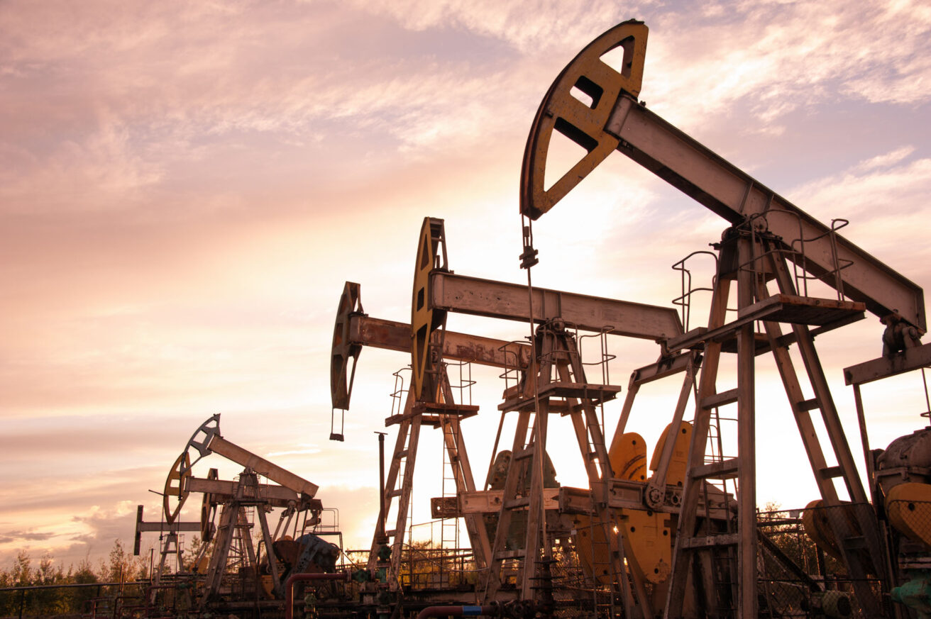 Oil pumpjacks operating in an oil field at sunset, with a cloudy sky in the background.