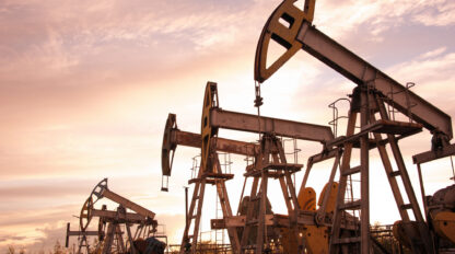 Oil pumpjacks operating in an oil field at sunset, with a cloudy sky in the background.