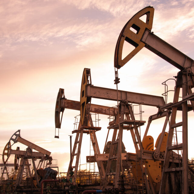 Oil pumpjacks operating in an oil field at sunset, with a cloudy sky in the background.