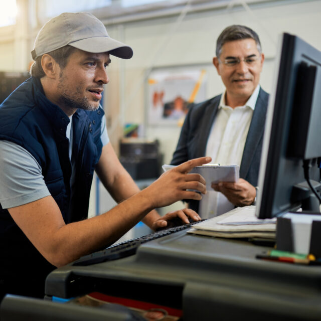 Auto repairman working on computer while talking with his manager in a workshop.
